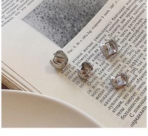 Detalle macro de pendientes geométricos plateados sobre libro con luz de ambiente