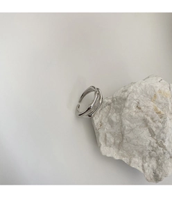 Detalle de anillo abierto plateado con ondas irregulares sobre una piedra blanca
