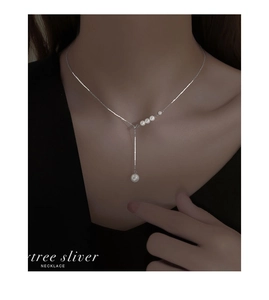 Gros plan d'un collier de perles argenté en forme de Y sur le cou d'un mannequin femme