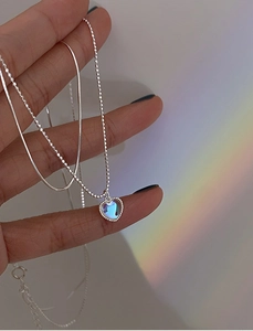 Detail of layered silver necklaces featuring heart moonstone pendant and elegant snake chains