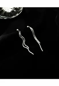 Vue détaillée de boucles d'oreilles pompon argentées avec chaînes ondulées sur tissu noir