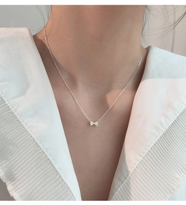Détail du collier pendentif nœud en argent avec zircons sur un chemisier blanc