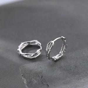 Pendientes de aro plateados con textura de espinas para mujer en fondo de piedra
