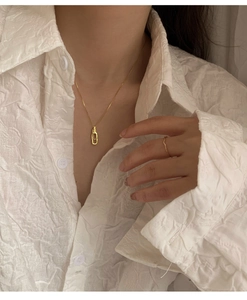 Nahaufnahme einer goldene geometrischen Halskette und Ring auf weißer Bluse