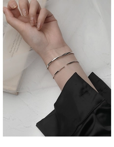 Detalle de brazaletes Mobius de plata minimalistas con diseño ondulado en muñeca mujer
