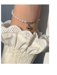 Detail of silver heart charm bracelet featuring freshwater pearls and linked metal chain