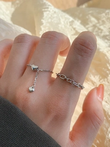 Detail of silver heart charm chain rings and thick link ring on a female finger