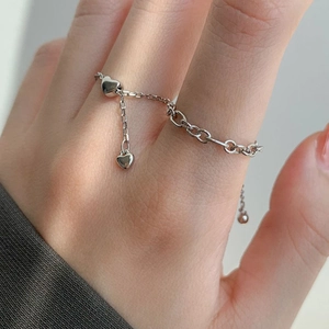 Minimalist silver chain ring with dangling heart charms worn on a finger
