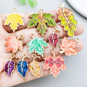 Pendentifs feuilles d'érable colorés en alliage doré tenus en main pour bijoux DIY