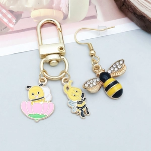 Detailansicht gelber Emaille-Bienenanhänger und goldener Schlüsselanhänger mit Strass