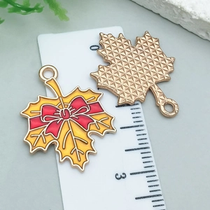 Detail of yellow maple leaf enamel pendant with red bow and gold textured back on scale