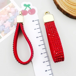 Detalle de colgante de llavero con diamantes rojos y cierre dorado junto a una regla