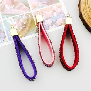 Detalle de llaveros con pedrería en forma de gota en violeta, rosa y rojo con clips dorados