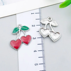 Detail view of red cherry alloy charms with green leaves and dimensions shown on a ruler