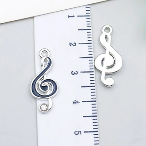 Detail of silver G-clef musical pendants with blue enamel and crystal inlay beside a ruler