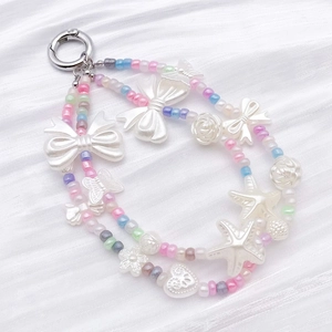 Détail de breloques en perles ABS avec papillons et fleurs sur un tissu plissé blanc