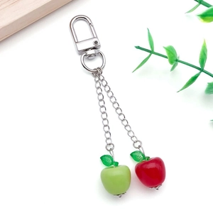 Detail of red and green acrylic apple pendants with silver lobster clasp on white background