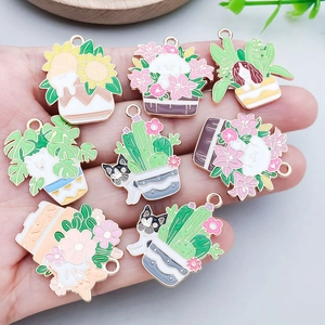 Handheld view of cartoon enamel pet and potted plant charms for DIY jewelry making