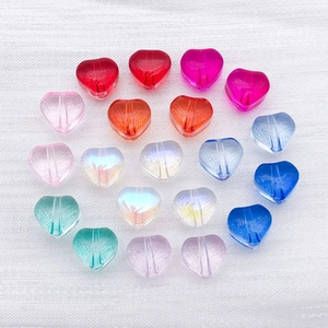 Perles en verre colorées en forme de cœur pour bijoux DIY disposées sur tissu blanc