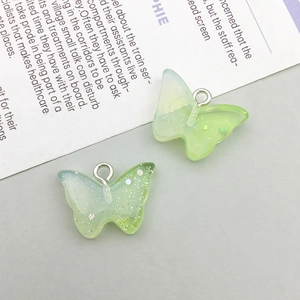 Macro detail of two light green translucent resin butterfly pendants with glitter and metal rings