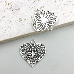 Macro shot of two vintage silver hollow heart charms with intricate butterfly motifs