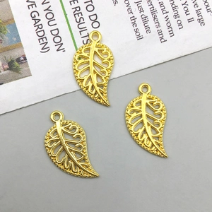 Three gold hollow leaf charms with loop hangers for DIY jewelry making on matte surface