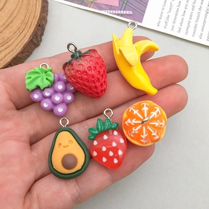 Hand holding assorted cute resin fruit pendants including strawberry and banana charms