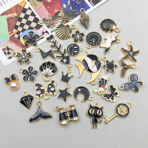 Flat lay of black and gold enamel alloy charms for DIY jewelry making on gray background