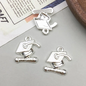 Macro view of three silver alloy graduation cap and diploma charms for DIY jewelry making