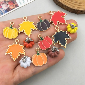 Bunte Ahornblatt- und Kürbisanhänger aus Emaille in der Hand für DIY-Schmuck