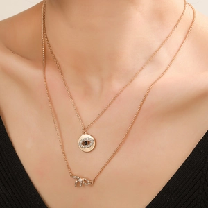 Collier double rang doré avec pendentif œil et nœud serti de cristaux et perle