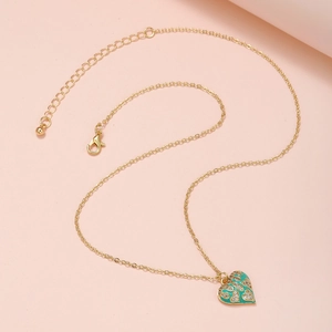 Detail eines Goldherz-Anhängers mit grüner Emaille und Zirkon-Inlay auf rosa Hintergrund