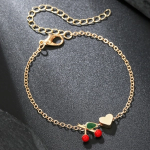 Macro detail of gold-plated chain featuring a red cherry charm and a polished heart pendant