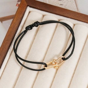 Handmade woven black rope bracelet with a polished gold U-link buckle in a jewelry box