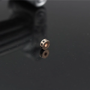Macro shot of rose gold spacer bead with black rhinestones on a reflective black background