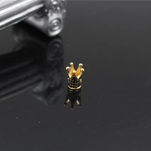 Golden crown jewelry charm with black micro-pave stones on reflective background