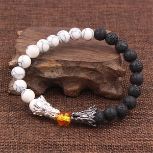 Dettaglio delle teste di drago su un bracciale in turchese bianco e pietra lavica nera