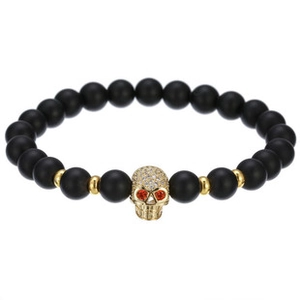 Detail of matte black stone bracelet featuring a gold skull charm with red gem eyes