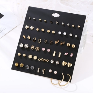 Close-up of 30 pairs assorted gold earrings set with pearls and rhinestones on black card