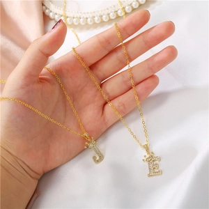 Close-up of golden crown initial J and E necklaces with zircon stones on silk background