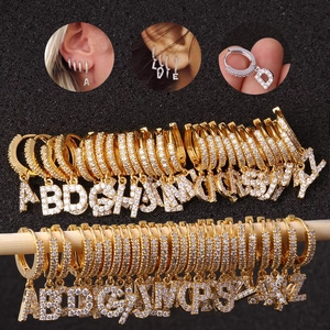 Macro detail of gold and silver huggie earrings with zircon-paved capital letter charms