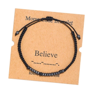 Detail of Morse Code bracelet with black cord and grey beads on craft card board