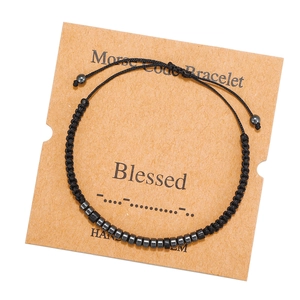 Macro shot of Blessed Morse code bracelet with black cord and metal beads on kraft card