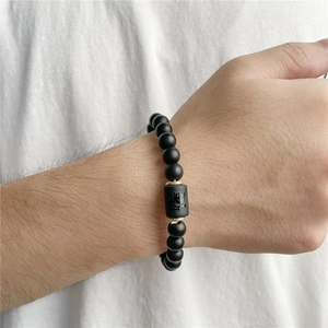 Detail of matte black onyx bead bracelet featuring a golden cylinder with dragon engraving