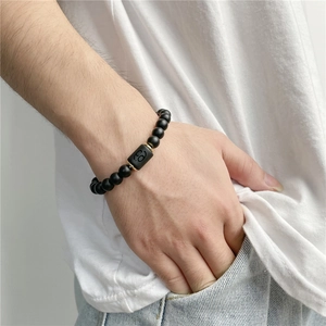 Close-up of matte black agate Cancer zodiac stretch bracelet on male wrist with gold spacers