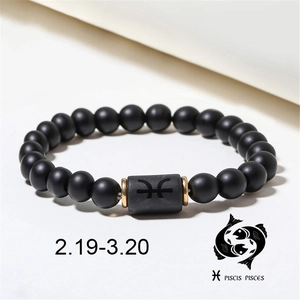 Macro detail of matte black onyx bead bracelet with Pisces zodiac symbol and gold rings