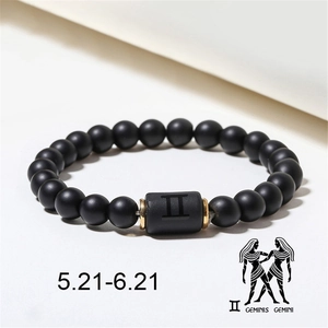 Close-up of matte black agate beads and Gemini zodiac symbol with gold accents