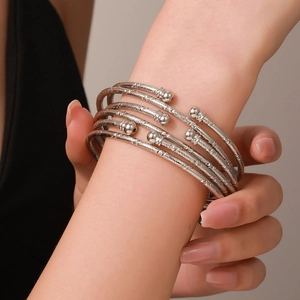 Detailweergave van vijf zilveren armbanden met spiraalstructuur op de pols van een vrouw