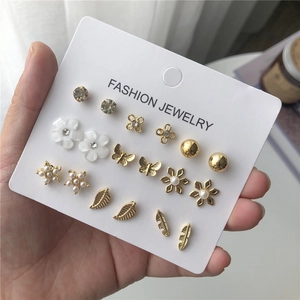 Mano sosteniendo juego de 9 pares de pendientes dorados con perlas y mariposas
