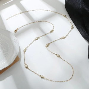 Collar largo dorado con colgantes geométricos y cierre ajustable sobre una superficie blanca
